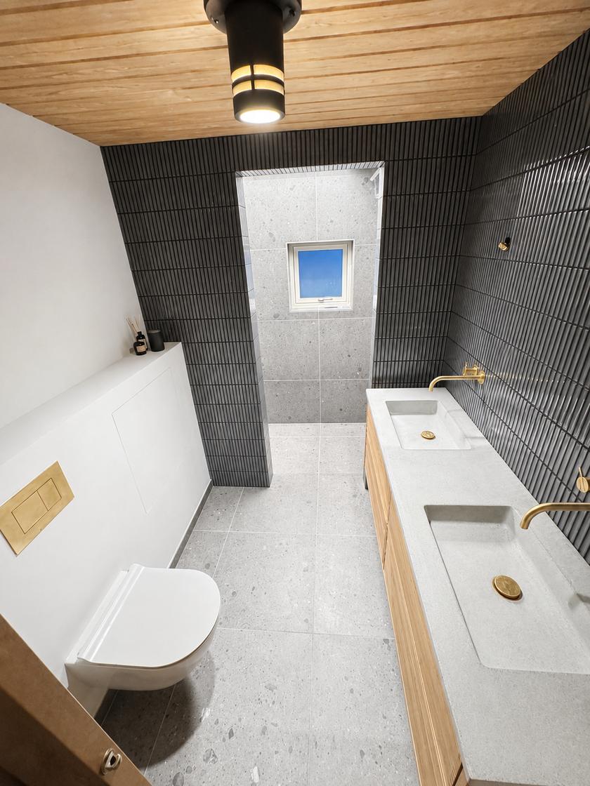 Moderne badeværelse med sorte fliser, træloft, dobbelt håndvask i beton-look med messingarmaturer og walk-in bruser